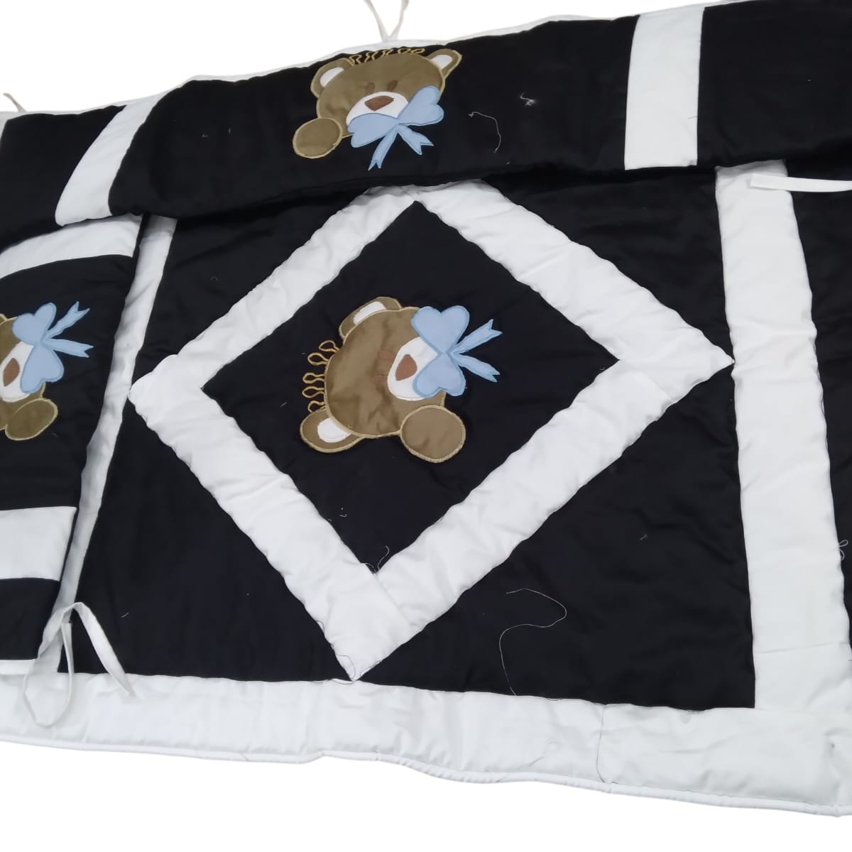 Close-up of black and white quilted baby set with embroidered teddy bear applique